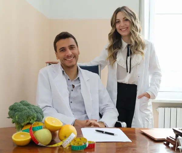 I due dietisti nello studio, alla scrivania con frutta e verdura