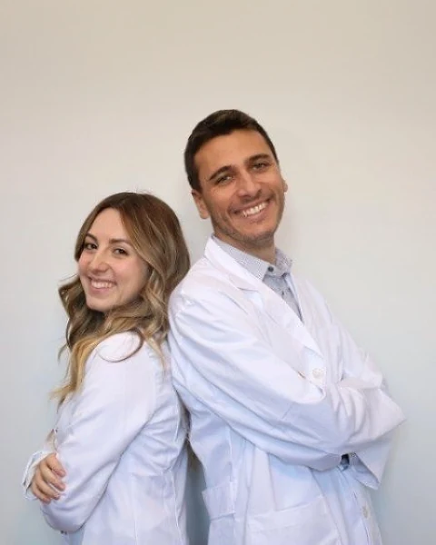La Dott.ssa Gaelle Melis e il Dott. Andrea Scrofani in camice, schiena contro schiena